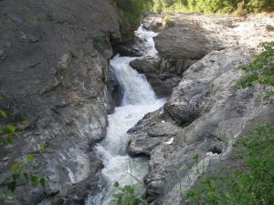 Cascada Putnei de la Lepșa, apă curgând printre stânci într-un defileu împădurit.